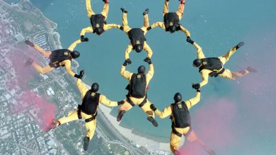 Åtta fallskärmshoppare gör en formation i luften som ser ut som två ringar som går in i varnadra.