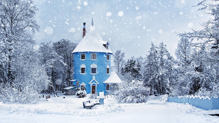 Muminhuset. Det är blått, runt och högt, som en cylinder. Det har en veranda och ett spetsigt tak. Huset och omgivningar är täckta av snö.