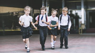 Fyra barn springer fram mot kameran. De har vita skjortor, svarta byxor eller kjolar och svarta blanka skor.