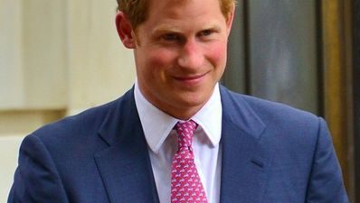 Prins Harry står i en blå kavaj och ser glad ut