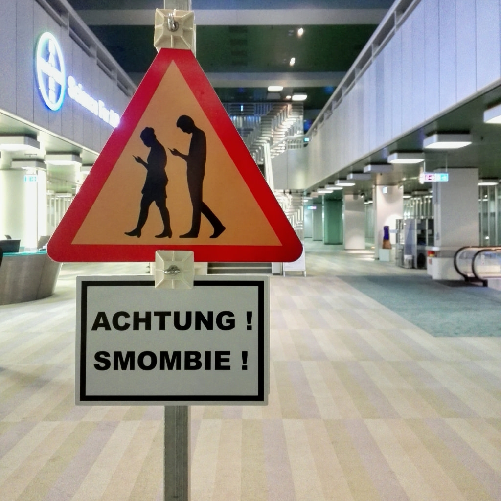 En varningsskylt med två människor som tittar ner i sina mobiltelefoner.