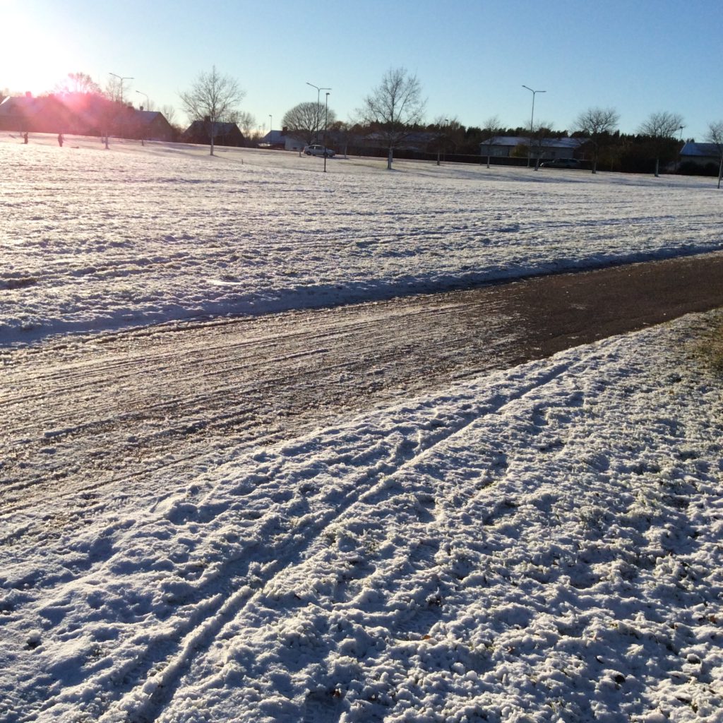 Bilden föreställer en cykelbana med snö på båda sidor. I övre, vänstra kanten skymtar solen.