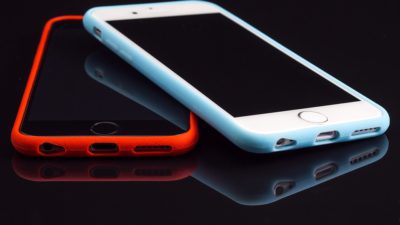 Två iPhones en med ett rött fodral och en med ett vitt fodral.