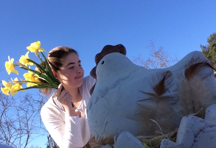 Ett barn håller i en bukett med påskliljor. I förgrunden en höna i porslin. Klarblå himmel.