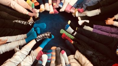 Barn sitter i ring med fötterna tillsammans. Strumporna har olika mönster och färger. Mattan under dem är mörkt blå.