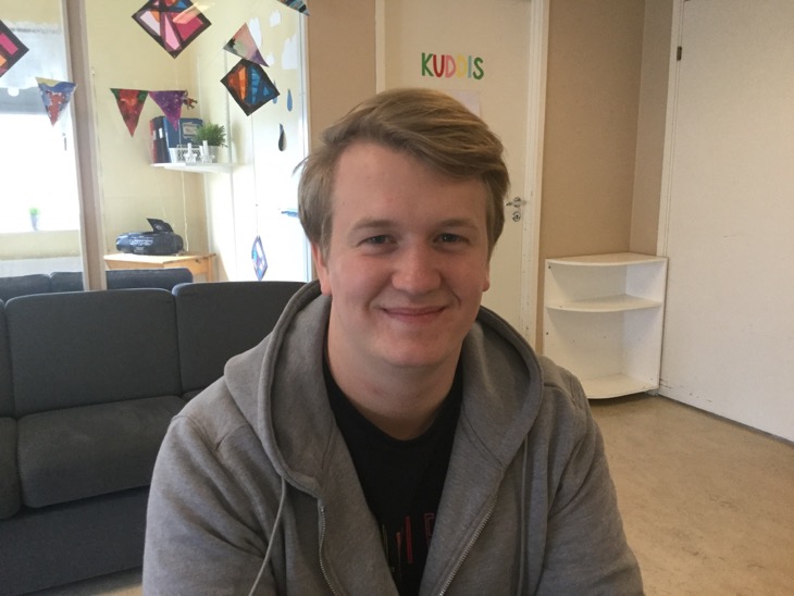 En person med grå munkjacka ler in i kameran.