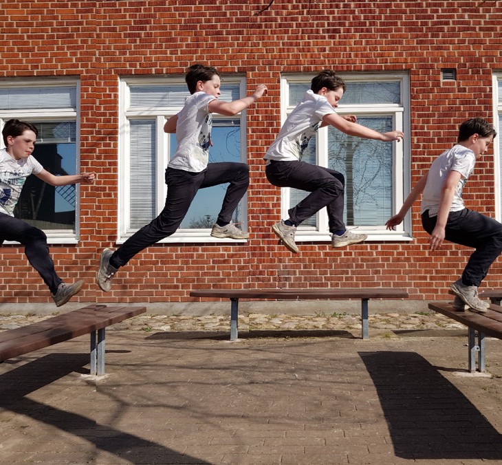 En skolelev hoppar mellan två bänkar. Vi ser honom på fyra olika ställen i luften.