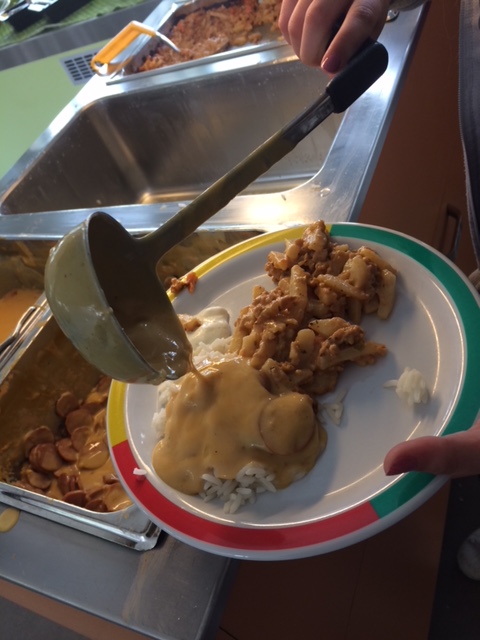 Mat läggs upp på en tallrik i en skolmatsal.