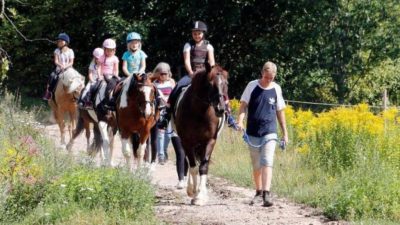 Fyra hästar går på led med barn som rider dem. Två vuxna leder hästarna.