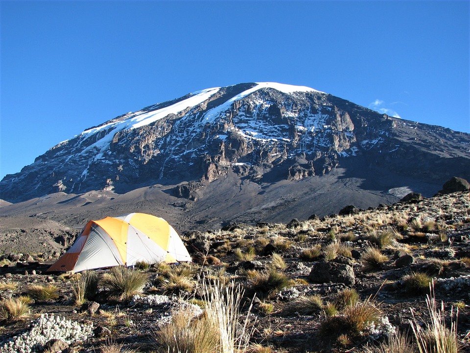 Berget Kilimanjaro är i bakgrunden. Framför Kilimanjaro är ett gult tält på en gräsplätt.