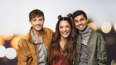 De tre programledarna står och håller om varandra och skrattar.