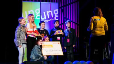 Sex elever står på scen. Några håller i en stor värdecheck och några håller i varsin ask med choklad.