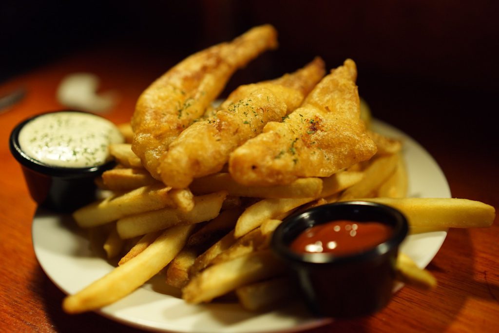 Friterade fiskbitar ligger på ett berg av pommes frites.
