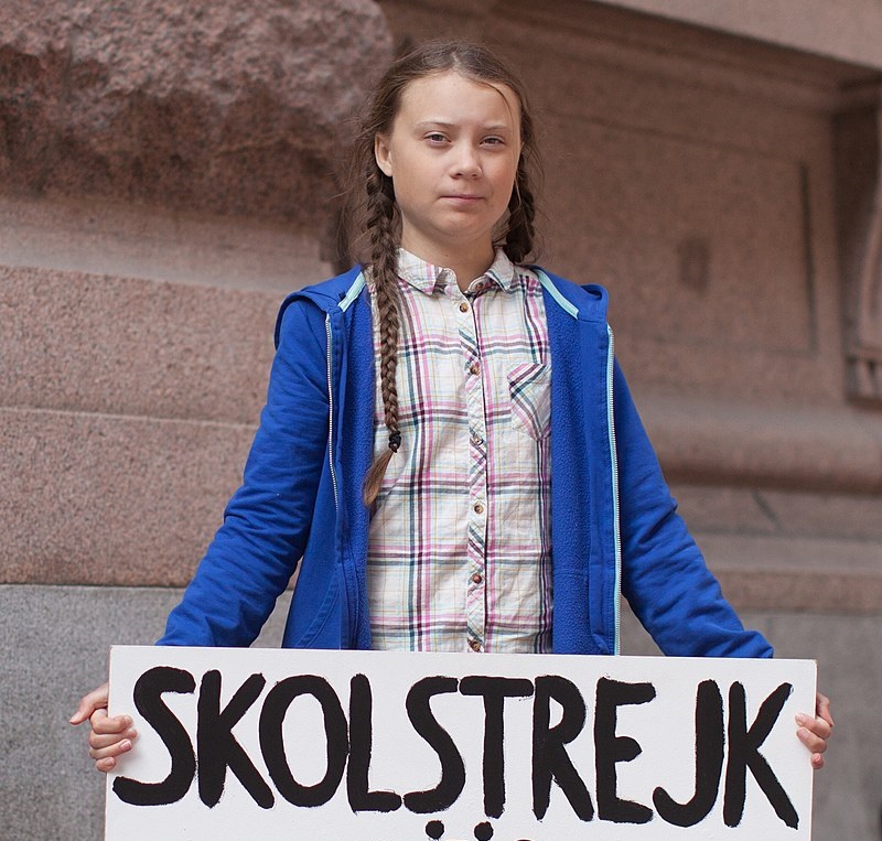 Greta Thunberg håller en skylt där det står skolstrejk för klimatet.