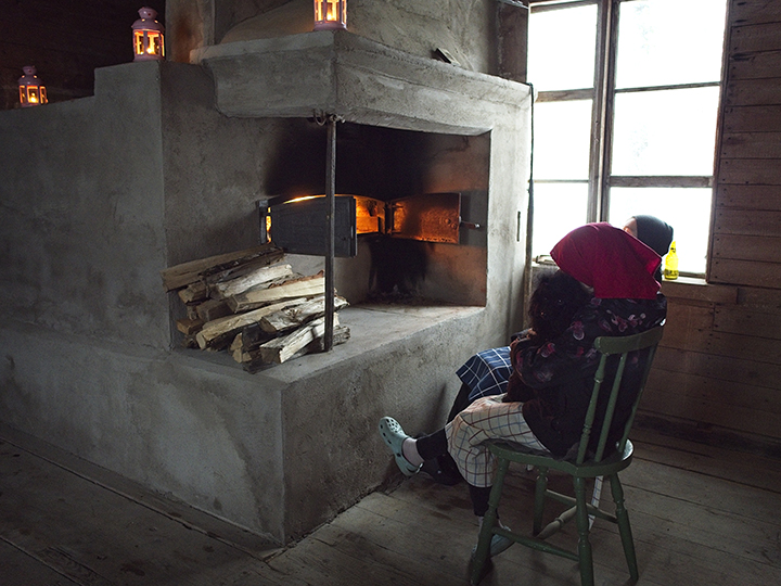 Två personer sitter framför en stor värmande bakugn.