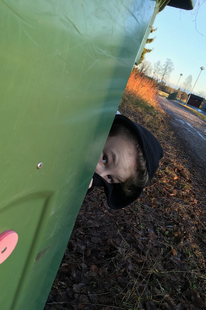 En kille tittar fram bakom ett sopkärl.